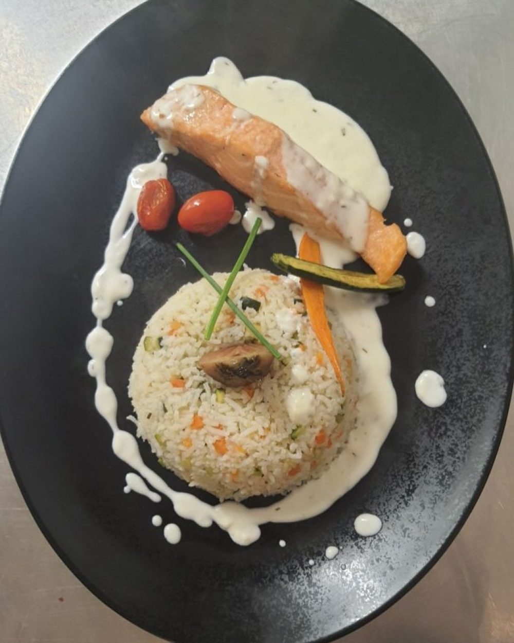 Un pavé de saumon avec un riz aux légumes et une sauce crémeuse, sur une assiette noire